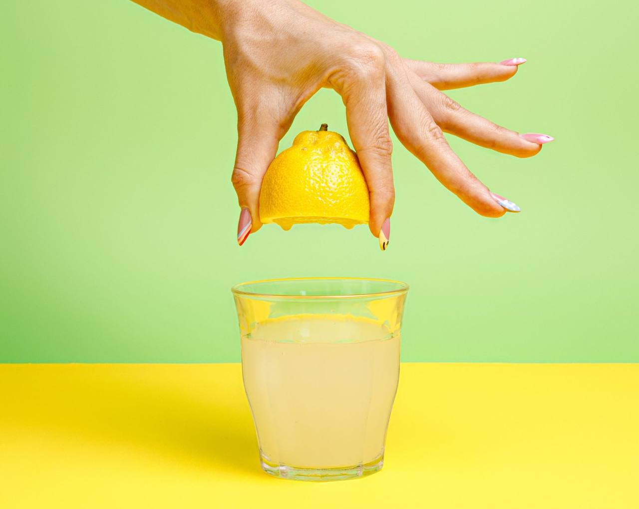 Mano exprimiendo medio limón sobre un vaso de limonada